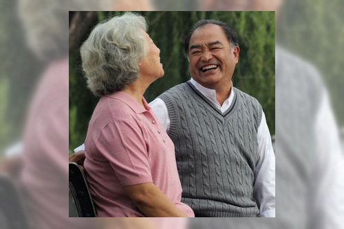 A senior man and woman sitting on a bench in the park laughing together