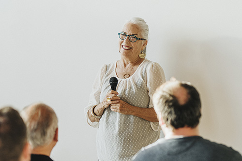 Older Adult woman holding a microphone and presenting in front of other older adults