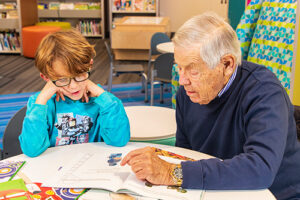 Oasis tutoring program featuring an older man with a young child reading