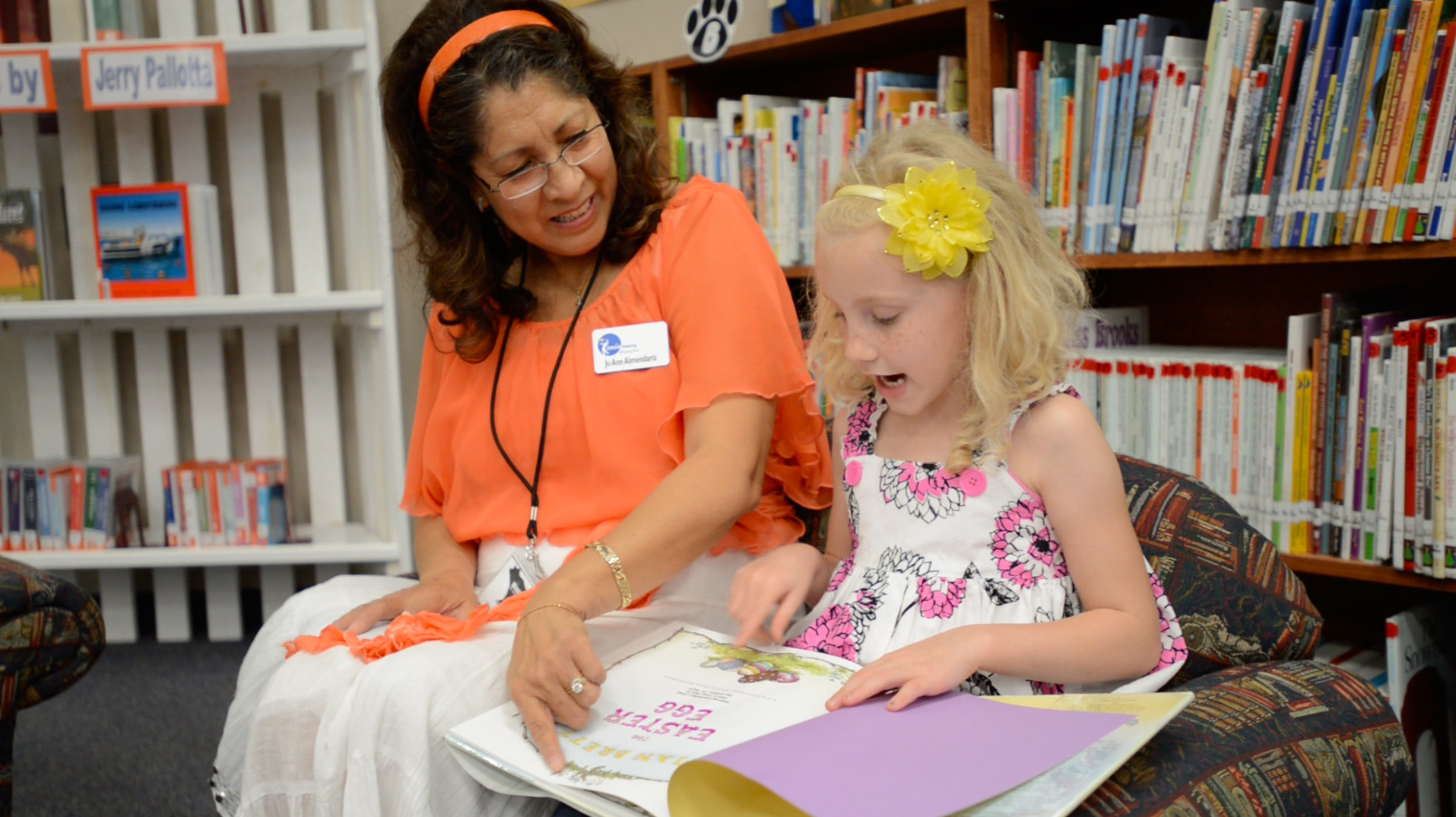 A woman tutoring a blonde child in a library setting