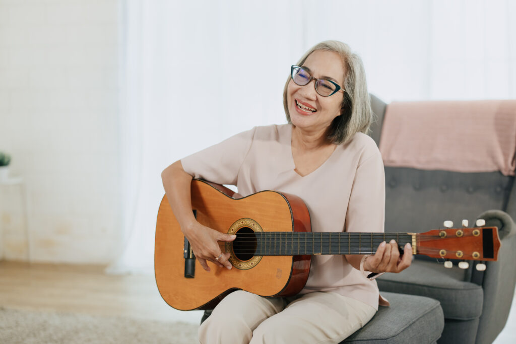 Healthy Senior Asian woman musician playing guitar music lover at living room indoors home.
